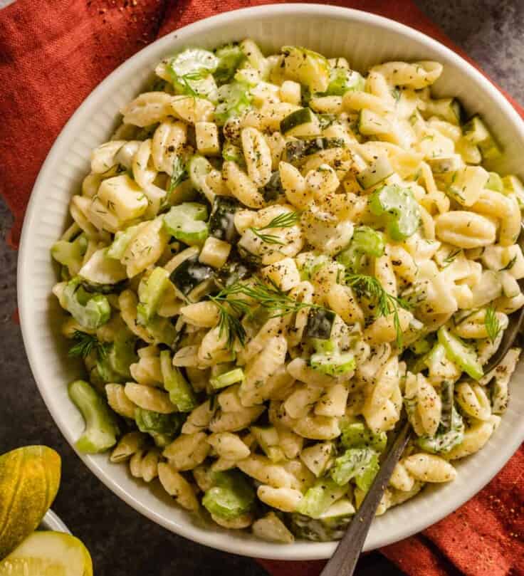 pasta salad in a white bowl with slices of celery and chunks of pickle in it