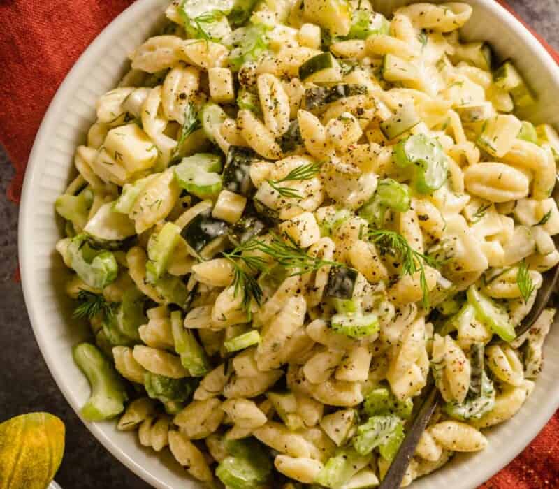 pasta salad in a white bowl with slices of celery and chunks of pickle in it