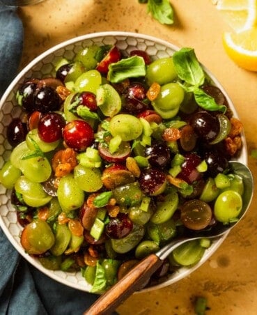 halved red and green grapes in a white bowl with a wooden spoon set in it