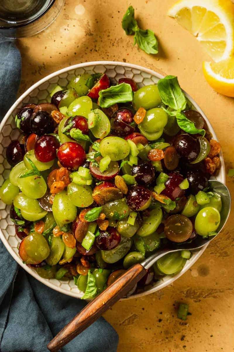 halved red and green grapes in a white bowl with a wooden spoon set in it