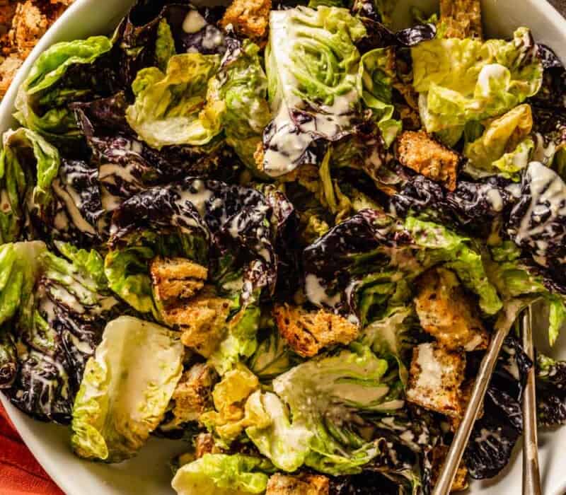 caesar salad with croutons in a large white bowl with two serving spoons set in it