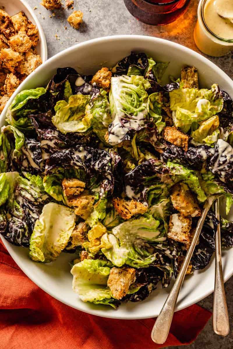 caesar salad with croutons in a large white bowl with two serving spoons set in it