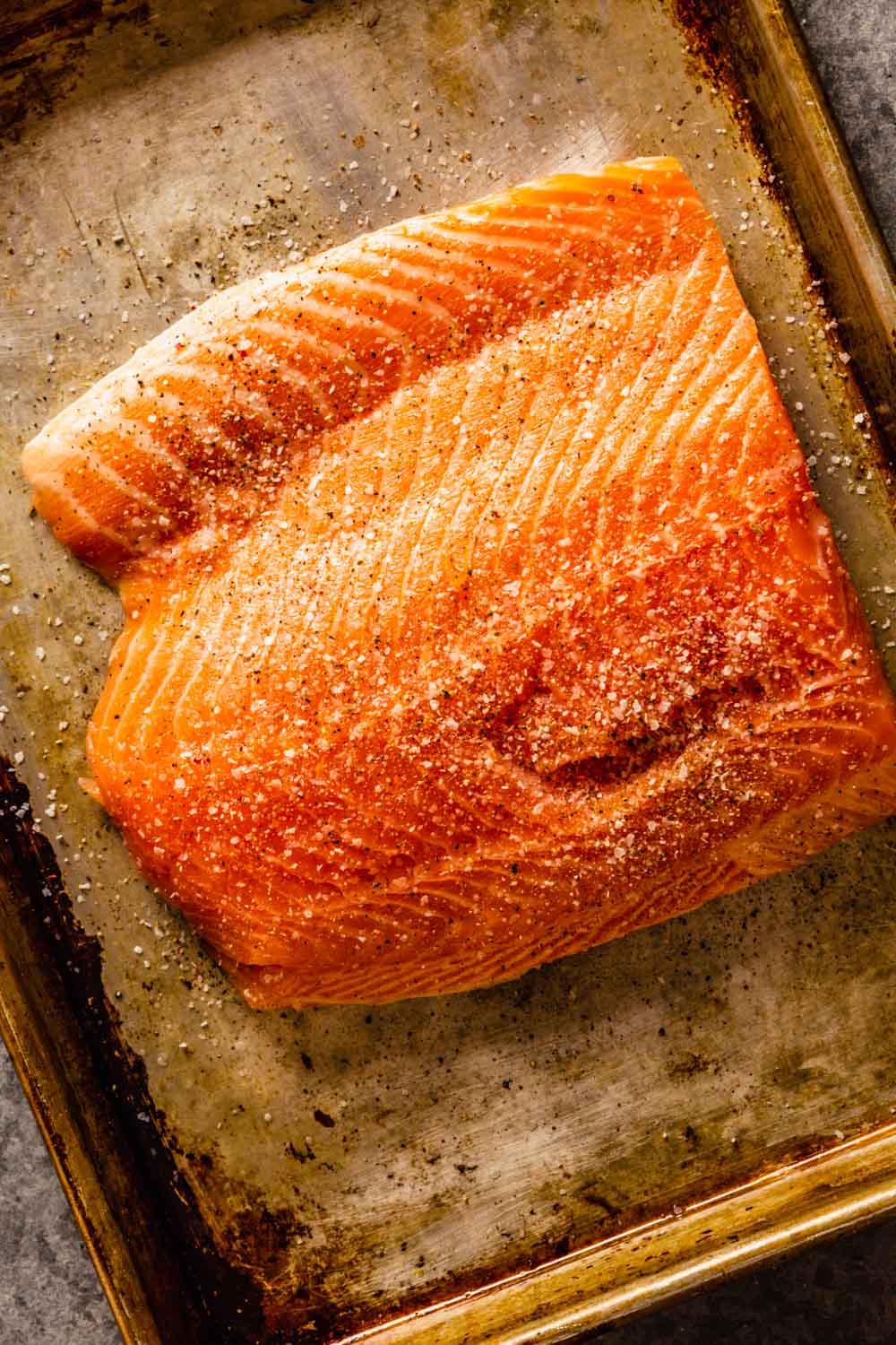 large salmon fillet on a baking sheet with salt and pepper sprinkled over top