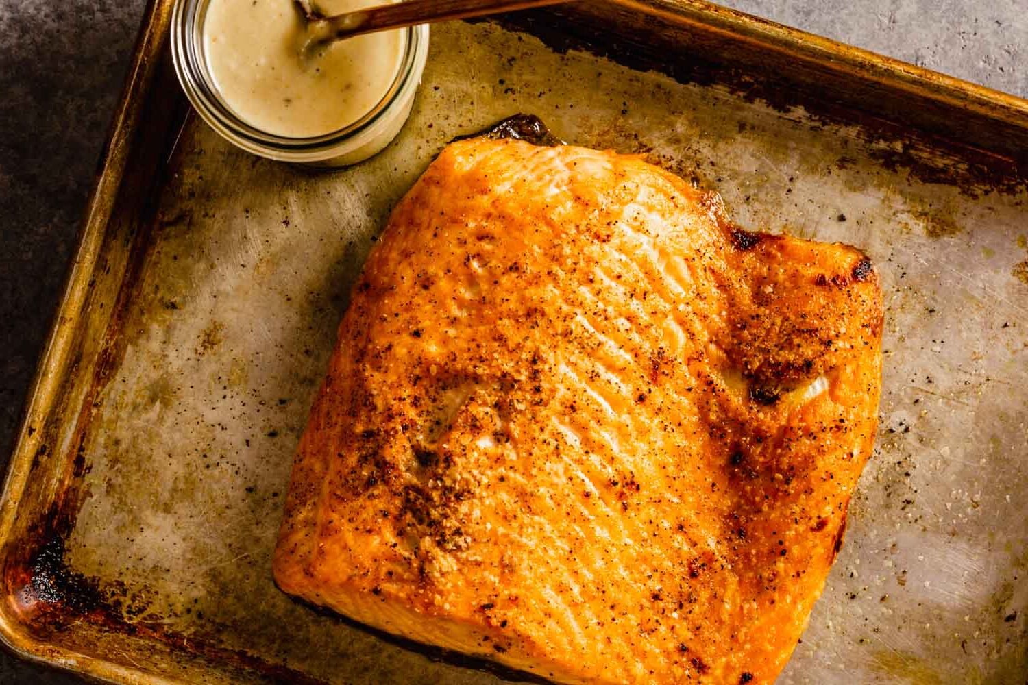 Broiled salmon on a baking sheet with a jar of caesar dressing set next to it. 