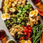 large bronze platter filled with cooked potatoes, tuna, cucumber chunks, halved cherry tomatoes, green beans, olives, soft-boiled eggs and fresh dill.