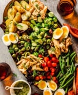 large bronze platter filled with cooked potatoes, tuna, cucumber chunks, halved cherry tomatoes, green beans, olives, soft-boiled eggs and fresh dill.