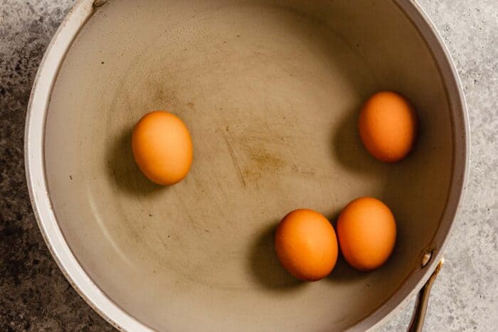 4 brown eggs in a large saute pan filled with water
