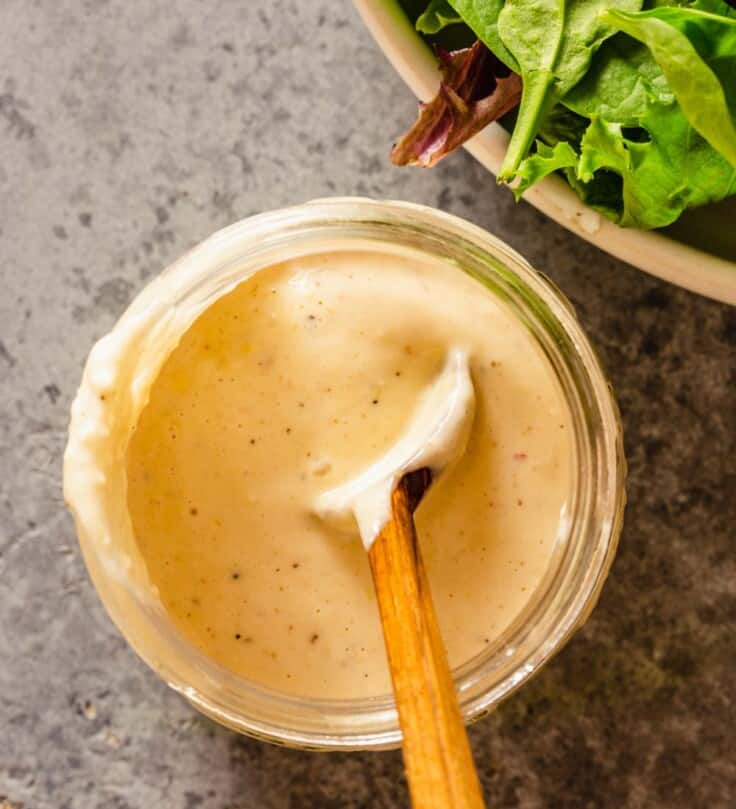creamy caesar dressing in a glass jar with a wooden spoon set in it