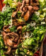 thin slices of steak on a bed of lettuce with herbs, sliced shallots and cucumber chunks.