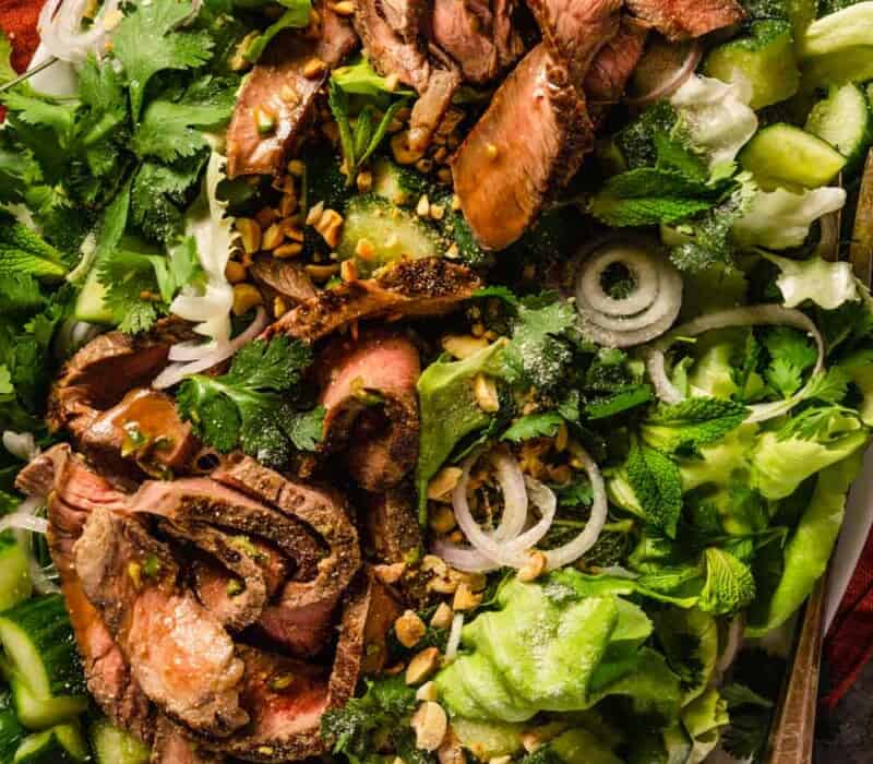 thin slices of steak on a bed of lettuce with herbs, sliced shallots and cucumber chunks.