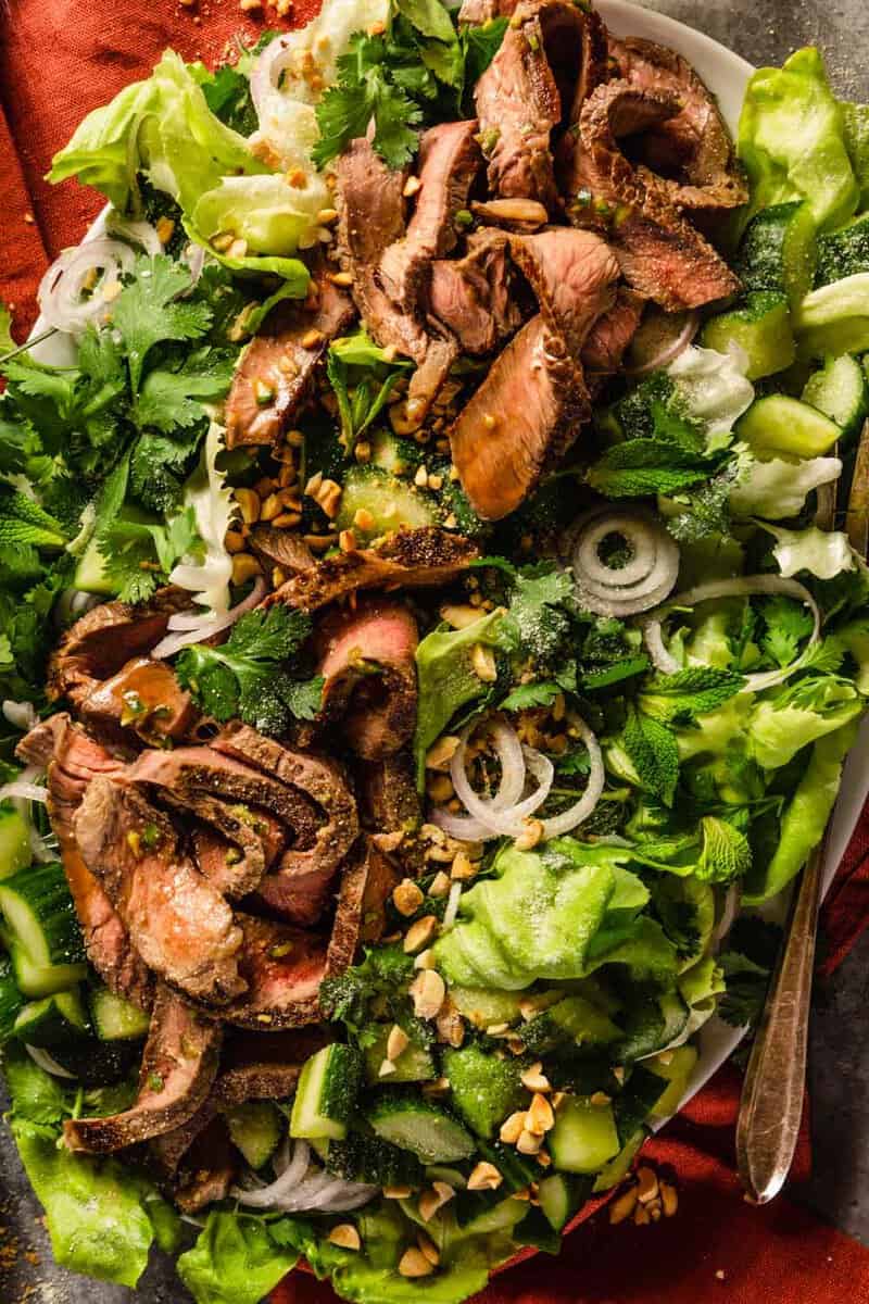 thin slices of steak on a bed of lettuce with herbs, sliced shallots and cucumber chunks. 