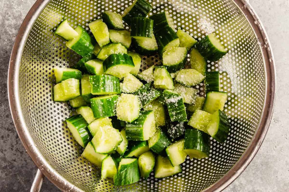 chunks of cucumber in a colander with salt sprinkled over top