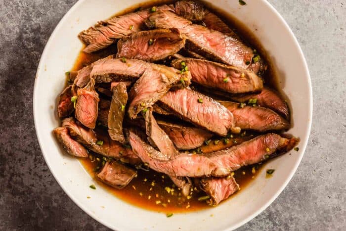 thin slices of steak in a large white bowl with a vinaigrette
