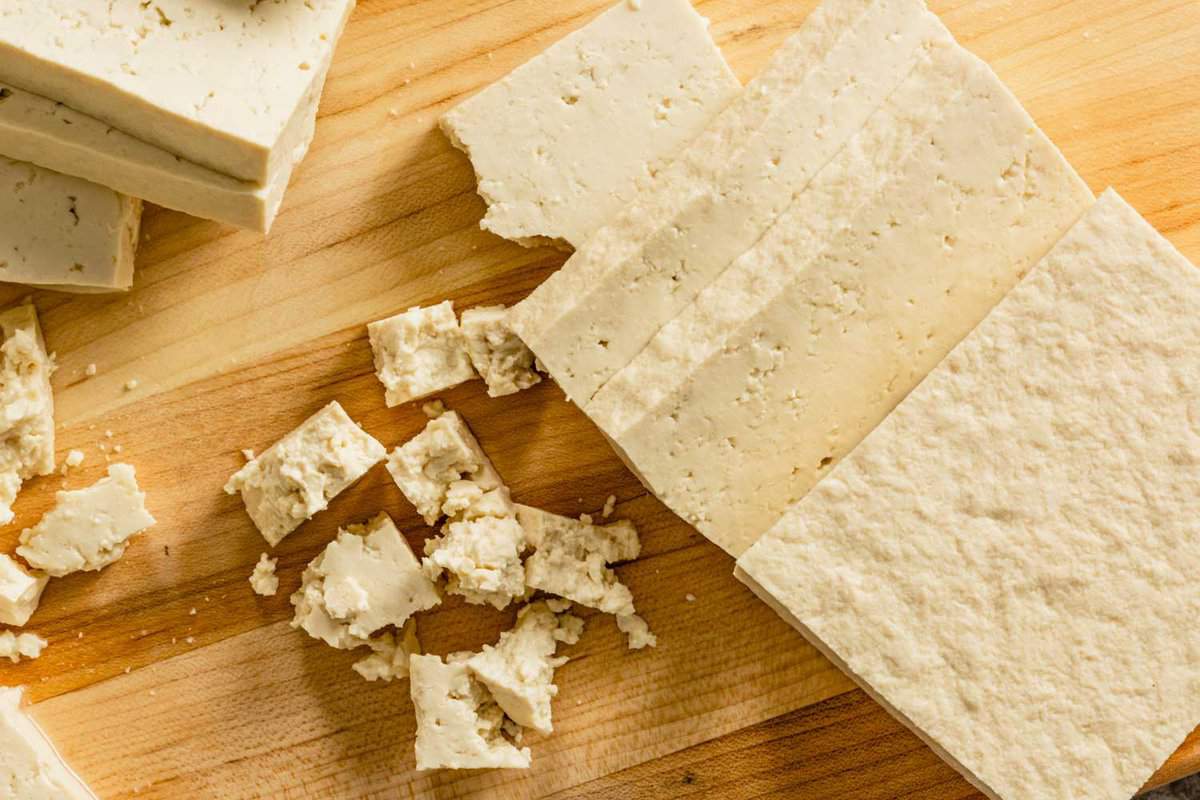 extra-firm tofu sliced and crumbled on a wood cutting board