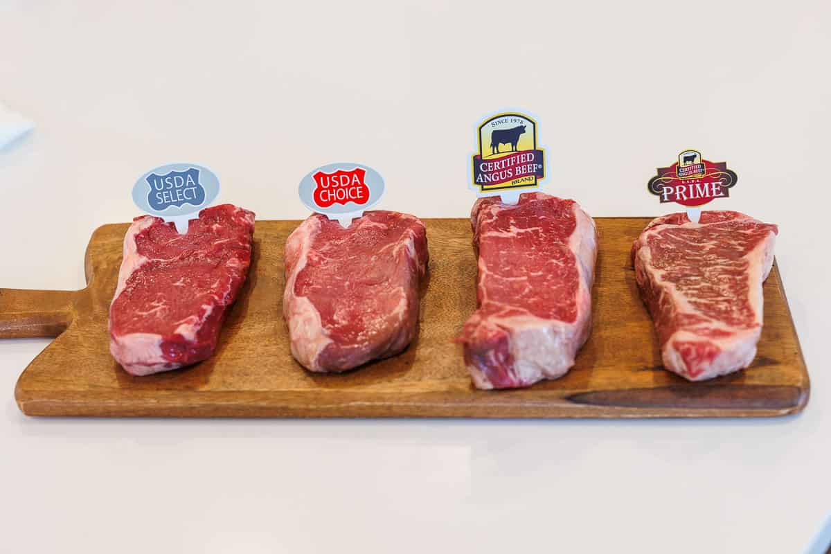 4 raw steaks set on a wood cutting board 