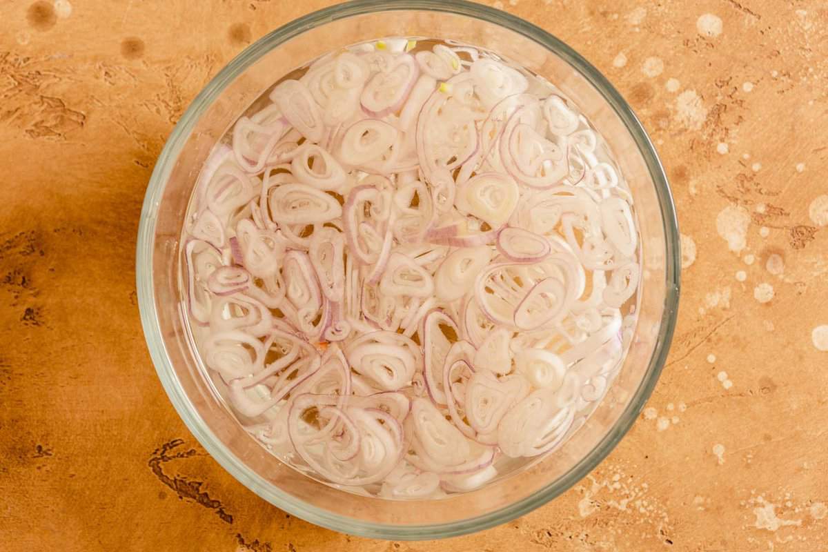 sliced shallots in a glass bowl filled with water