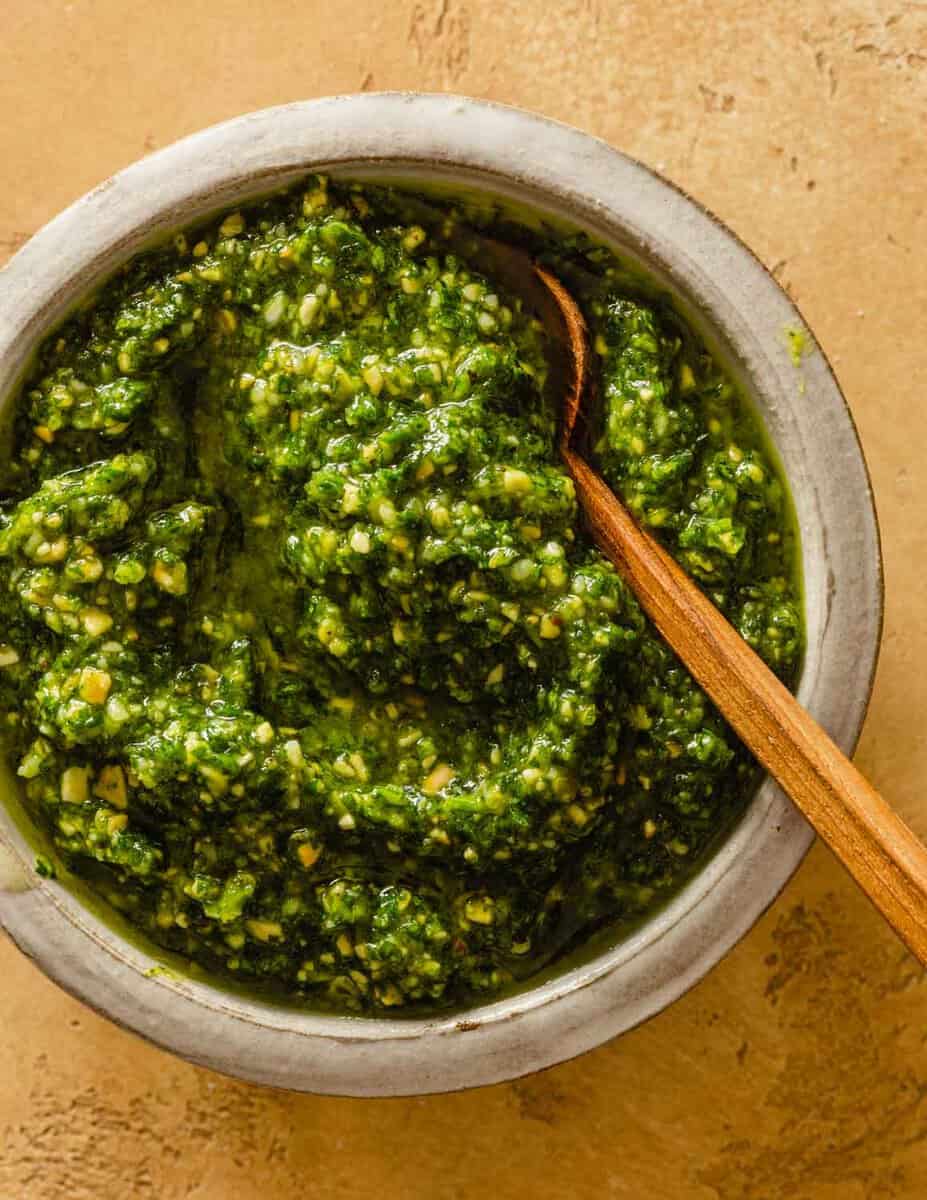 green pesto in a small white bowl with a small wooden spoon