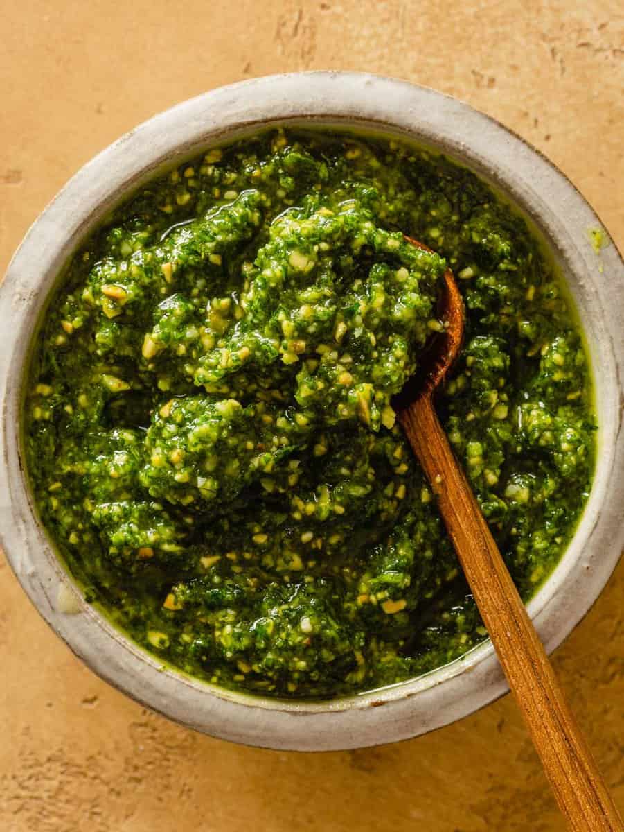 green pesto in a small white bowl with a small wooden spoon