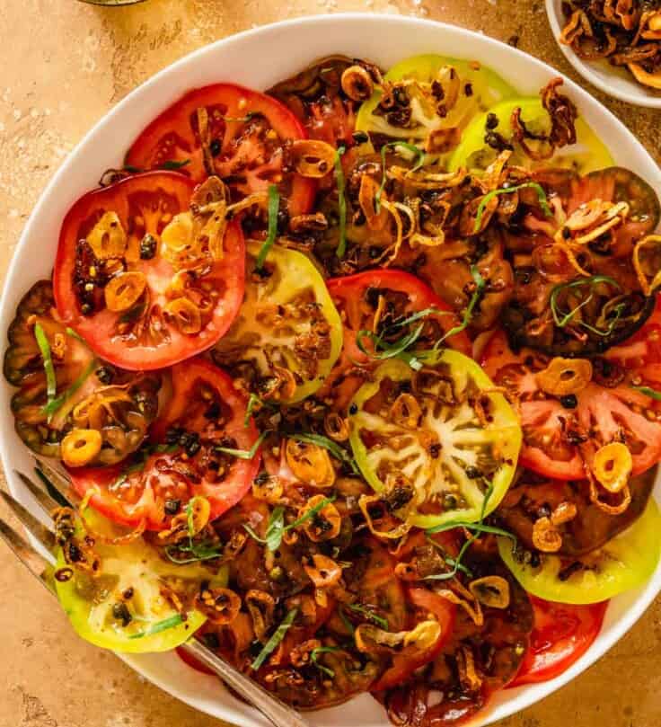 sliced multi-color tomatoes on a white plate with crispy browned shallots on top