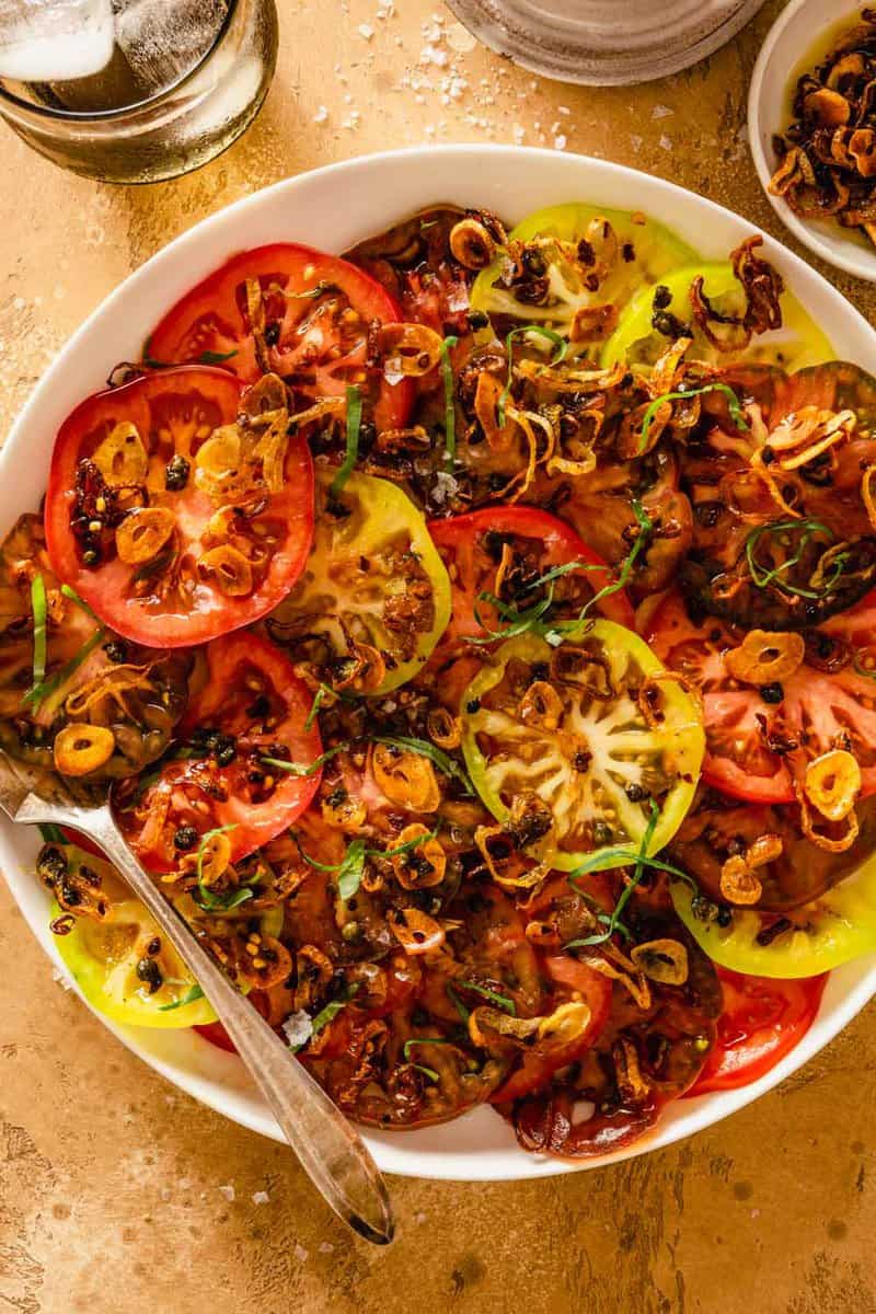 sliced multi-color tomatoes on a white plate with crispy browned shallots on top