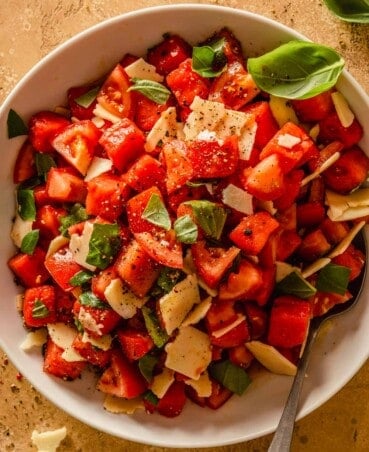 watermelon and tomato salad in a large white bowl with shreds of cheese and pieces of basil