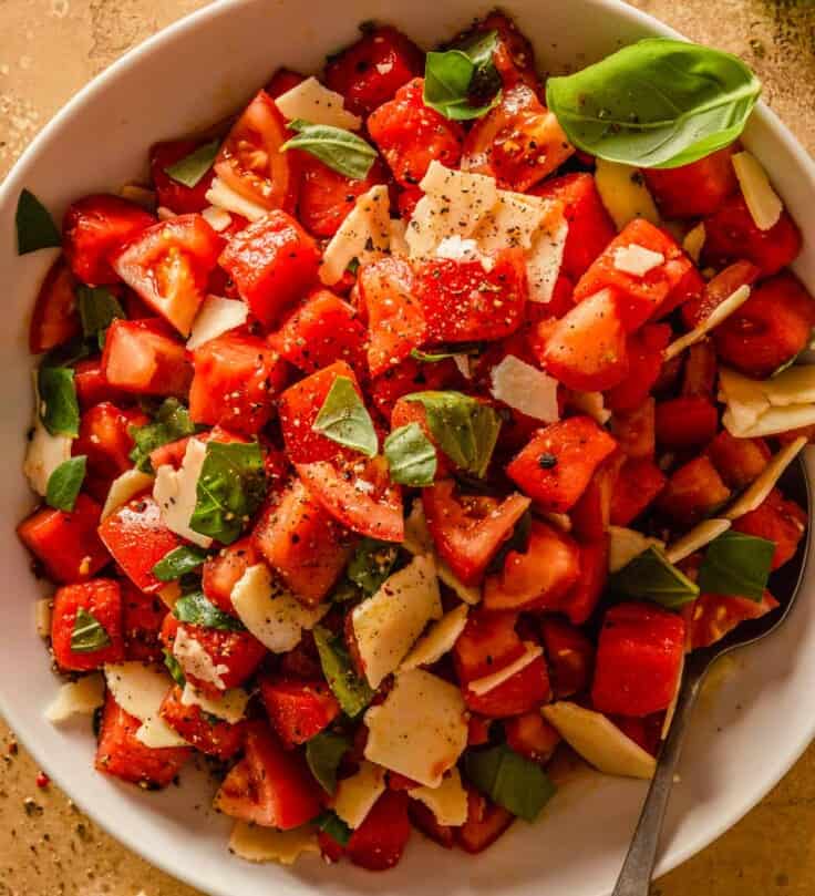 watermelon and tomato salad in a large white bowl with shreds of cheese and pieces of basil