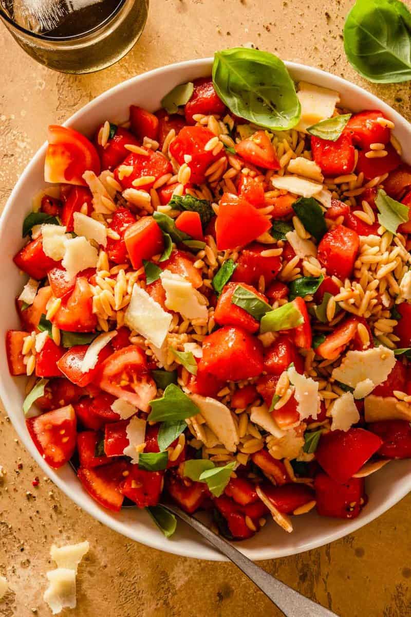 chunks of tomatoes and watermelon tossed with orzo pesto and basil in a large white bowl