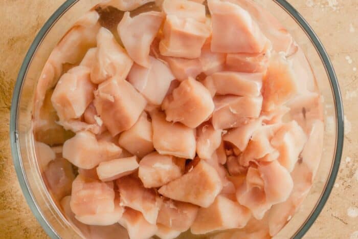 raw chunks of chicken breast in a large glass bowl filled with water