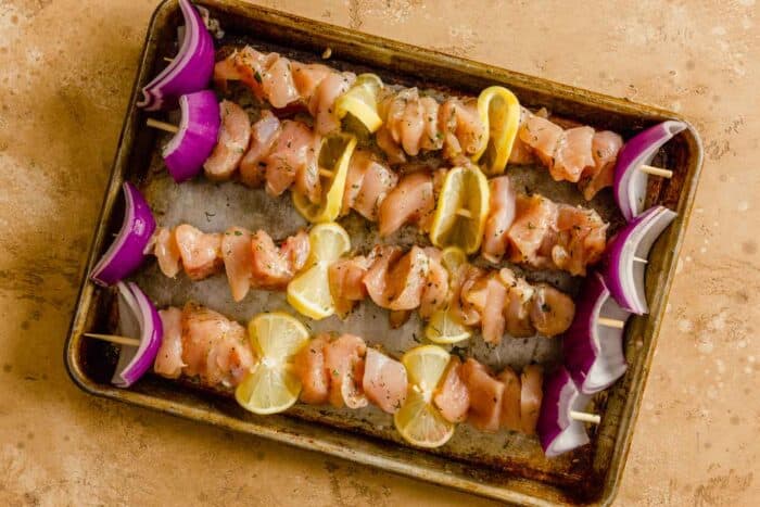 raw chicken threaded onto wooden skewers with lemon slices and red onion wedges