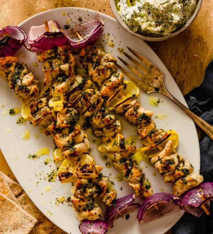 chicken skewers on a large oval white plate with red onions and lemon slices