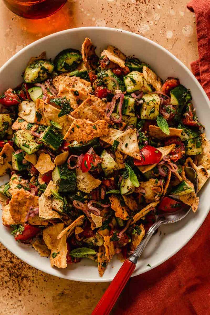 pita and vegetable salad in a shallot white bowl with a red-handled spoon set in it