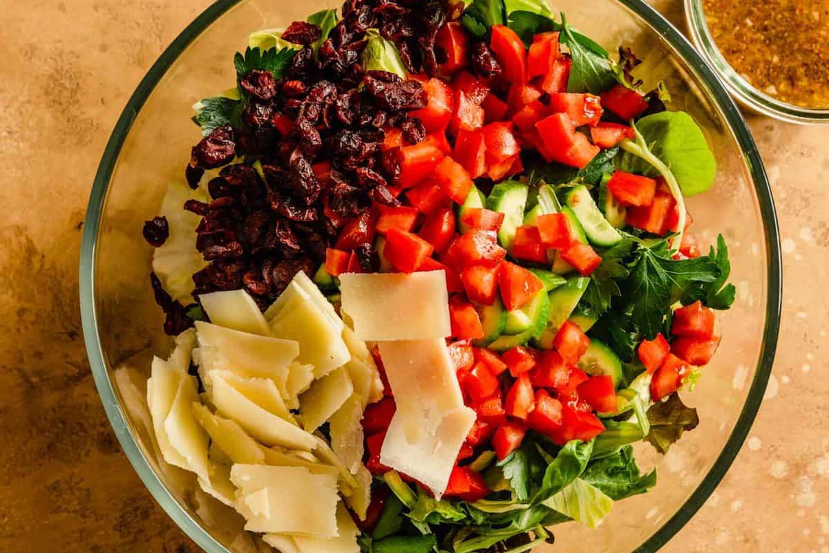 greens, cheese, tomatoes and cranberries in a large clear bowl