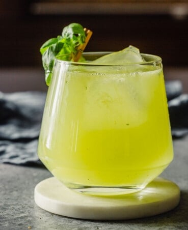 Yellow-ish green cocktail in a rocks glass garnished with a basil leaf.