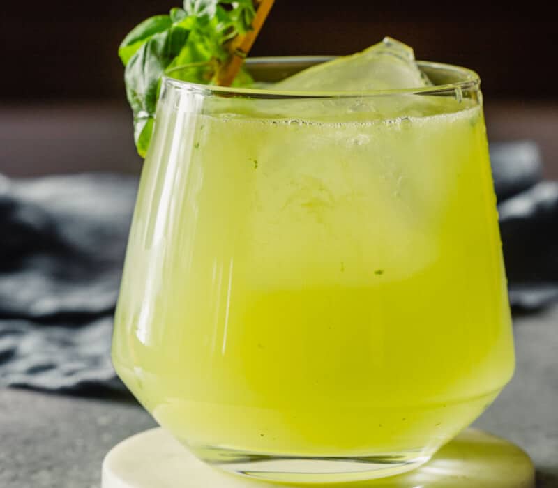 Yellow-ish green cocktail in a rocks glass garnished with a basil leaf.