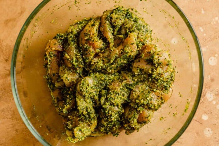 chicken tenders coated in pesto in a glass bowl