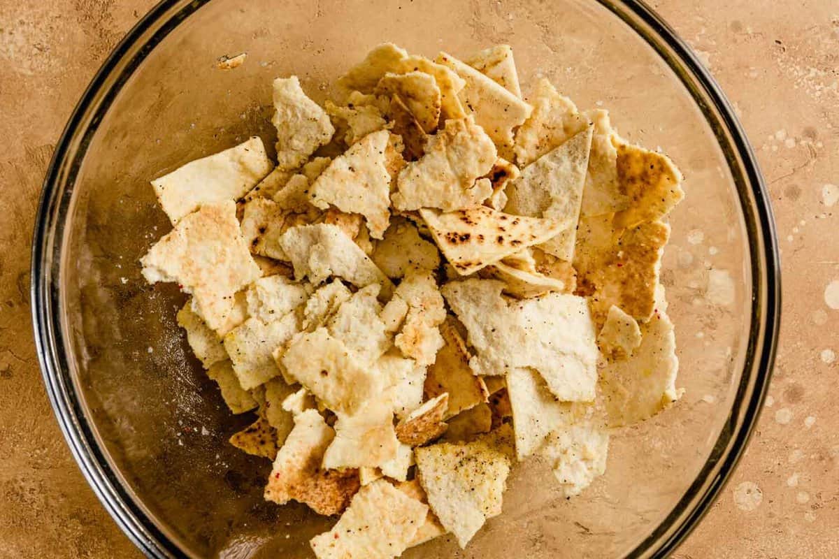 pieces of pita bread tossed in a glass bowl with oil, salt and pepper