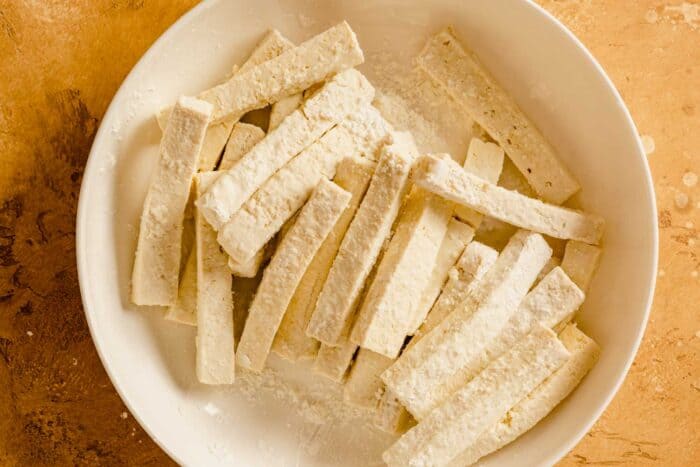 sticks of tofu coated in cornstarch in a white bowl