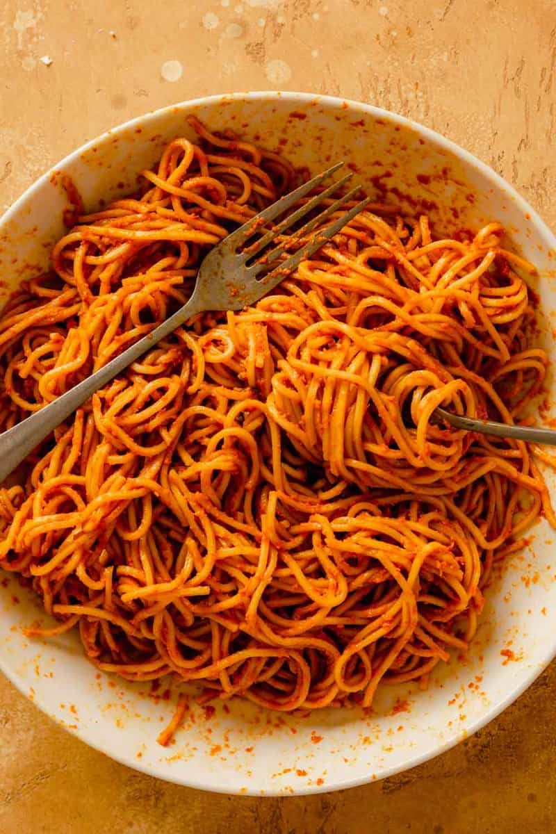 ramen noodles coated in a red sauce in a large white bowl with two forks