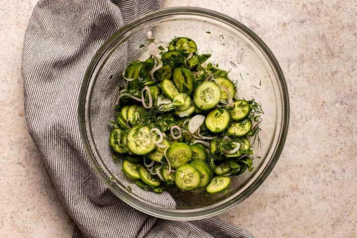 sliced cucumbers and herbs in a clear glass bowl