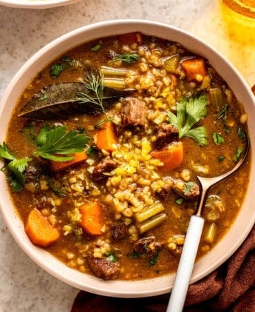 beef, barley and vegetable soup in a shallow white bowl
