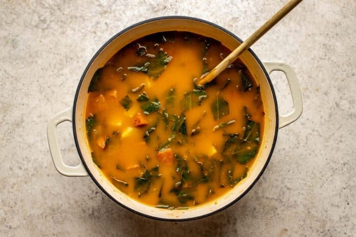 creamy orange-flavored soup with greens in a Dutch oven