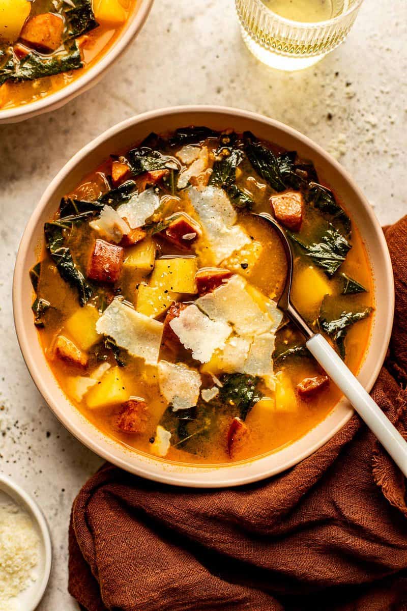 creamy soup with chunks of potato, sausage and greens in a shallow white bowl