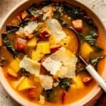 creamy soup with chunks of potato, sausage and greens in a shallow white bowl