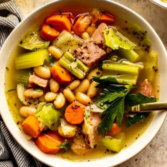 ham and white bean soup with chunks of carrots and celery in a shallow white bowl