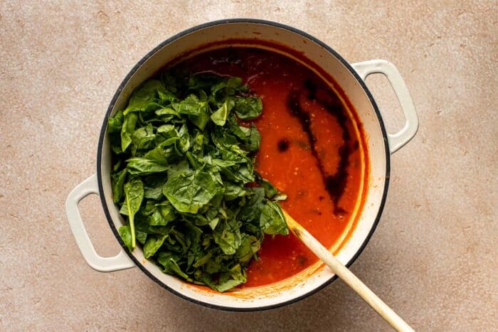 tomato soup and spinach in a white dutch oven