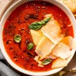 tomato soup in a shallow white bowl with parmesan and fresh basil on top