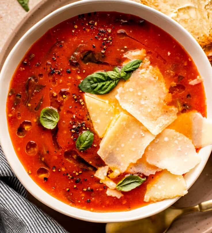 tomato soup in a shallow white bowl with parmesan and fresh basil on top