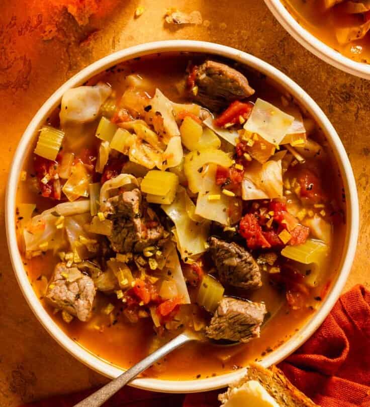 beef and cabbage soup with tomatoes in a shallow white bowl