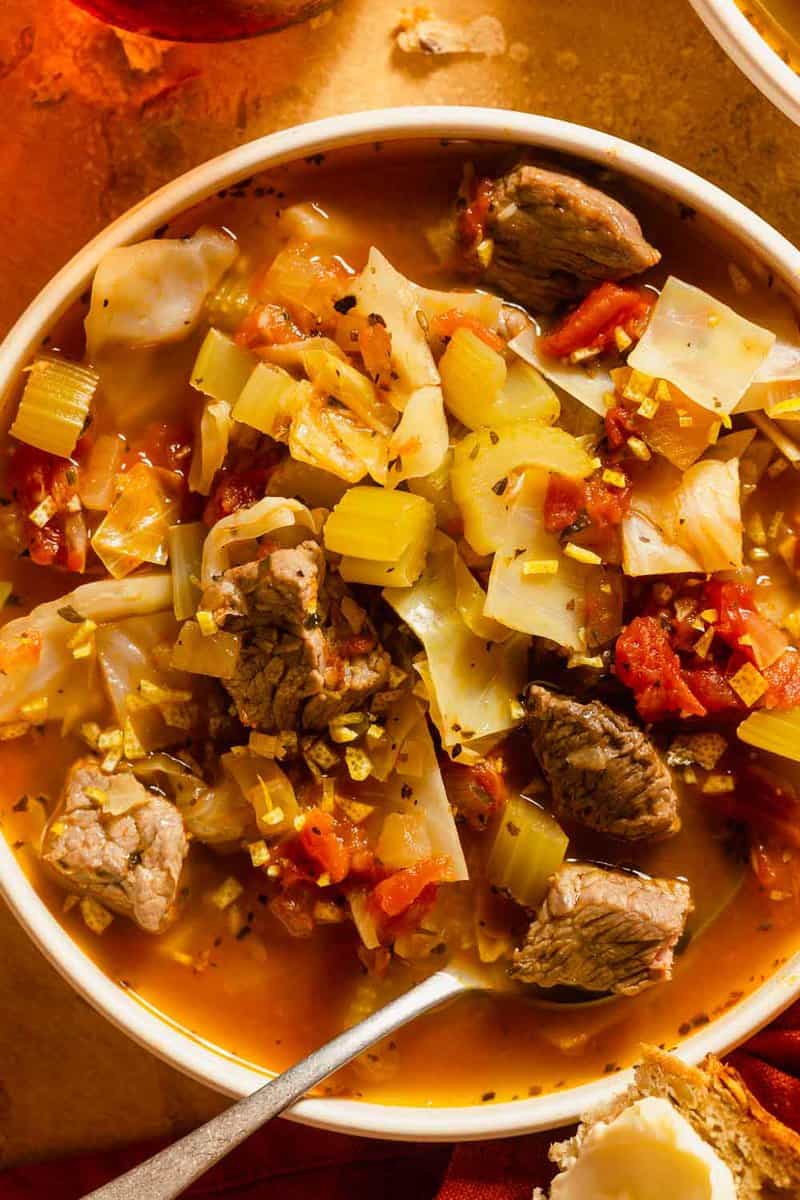 beef and cabbage soup with tomatoes in a shallow white bowl