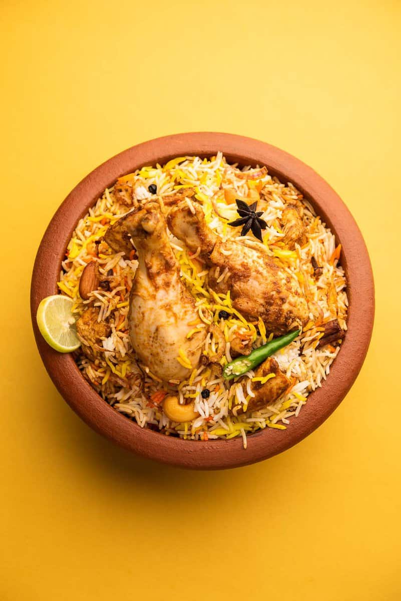 rice and chicken Indian dish in a orange bowl set on a yellow background
